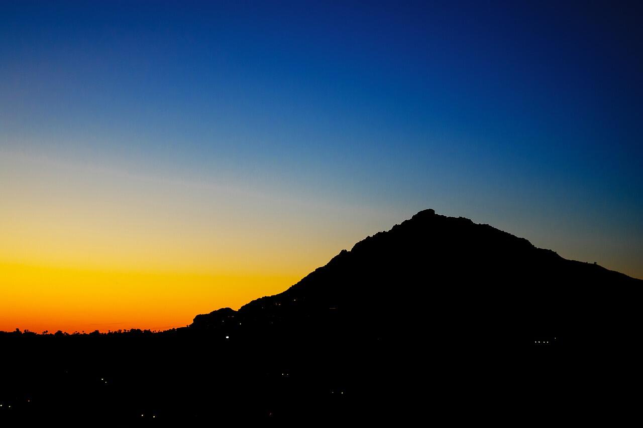 A desert mountain silhouetted against the sky above central Phoenix at dusk