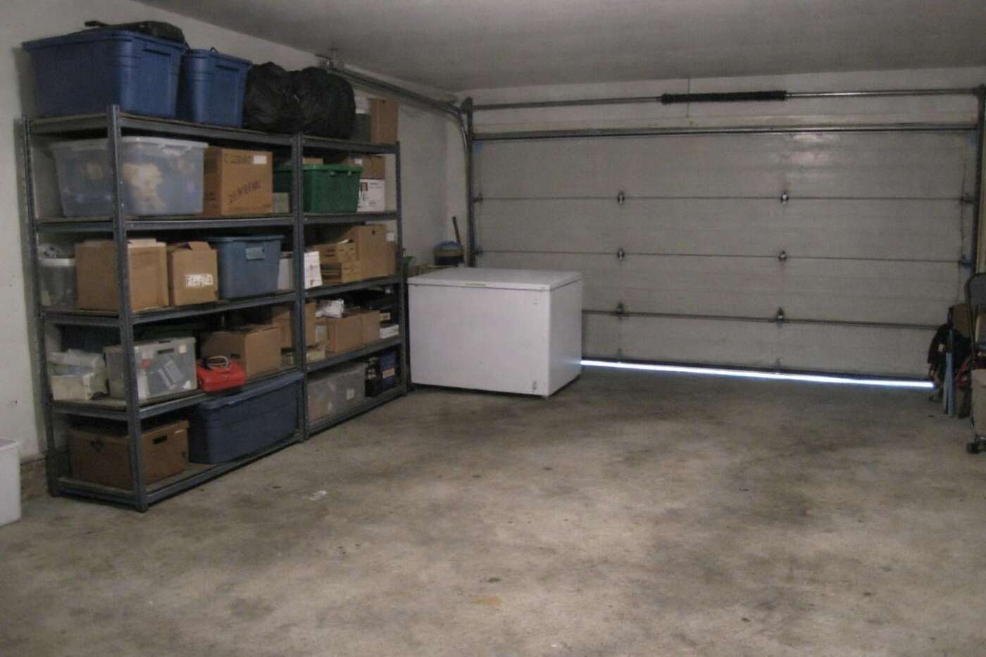The inside of a suburban garage with shelving, storage bins and a line of daylight under the door